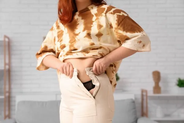 Image of woman trying to do her trousers up after pregnancy weight gain Felixstowe